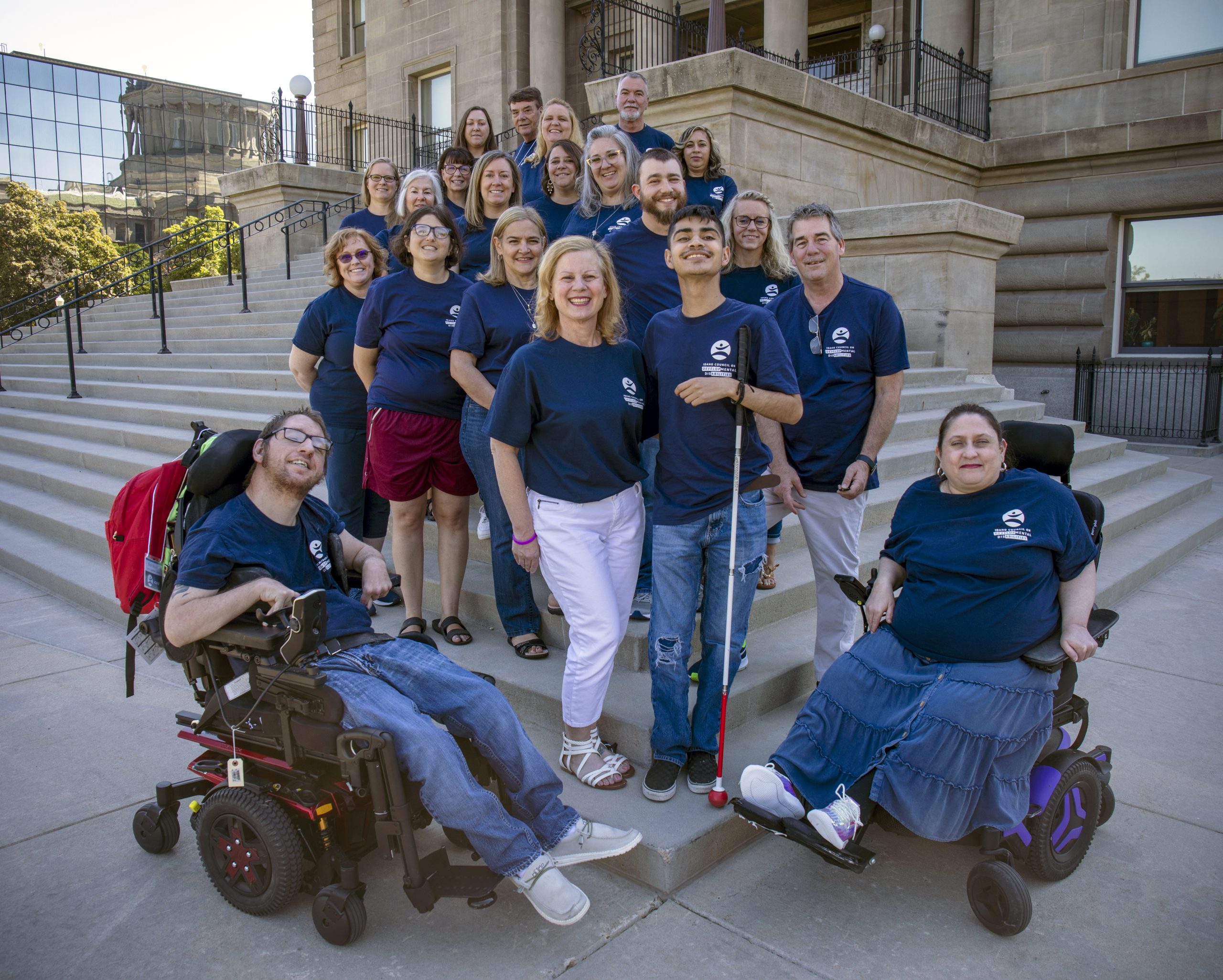 Idaho Council members wearing navy tshirts smiling in front of west stairs of capitol building